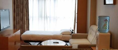A hotel room with a bed, a sofa, a small table, a television, and a water dispenser.