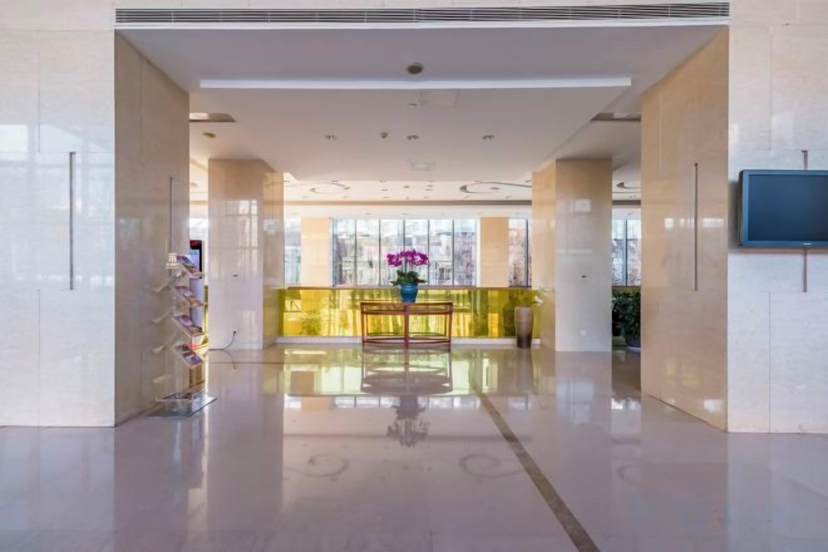 A spacious lobby with a polished floor, a reception desk, and a large window offering a view of the city.