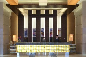 Un espace d’accueil comprenant un comptoir de réception, deux réceptionnistes et un aménagement moderne avec des luminaires verticaux.