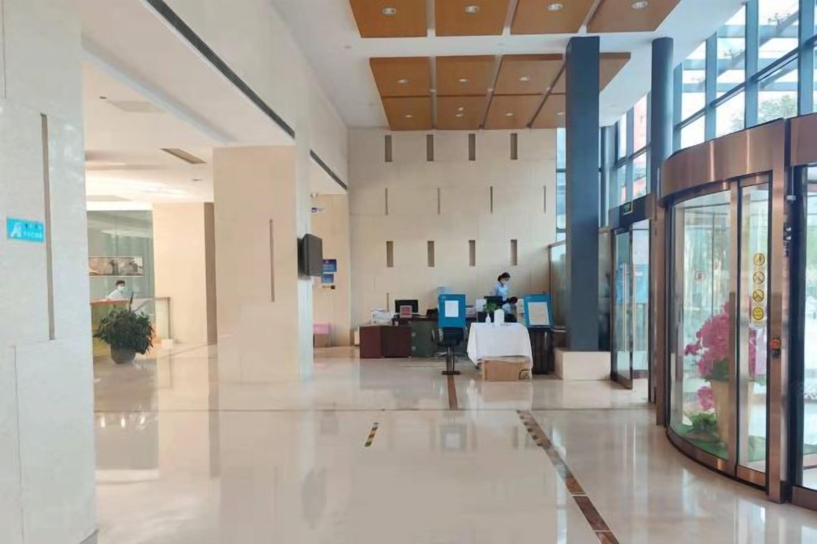 A hotel lobby with a reception desk, a plant, and a glass elevator.