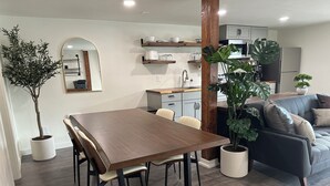 A modern living room with a wooden dining table, a sofa, and a potted plant.