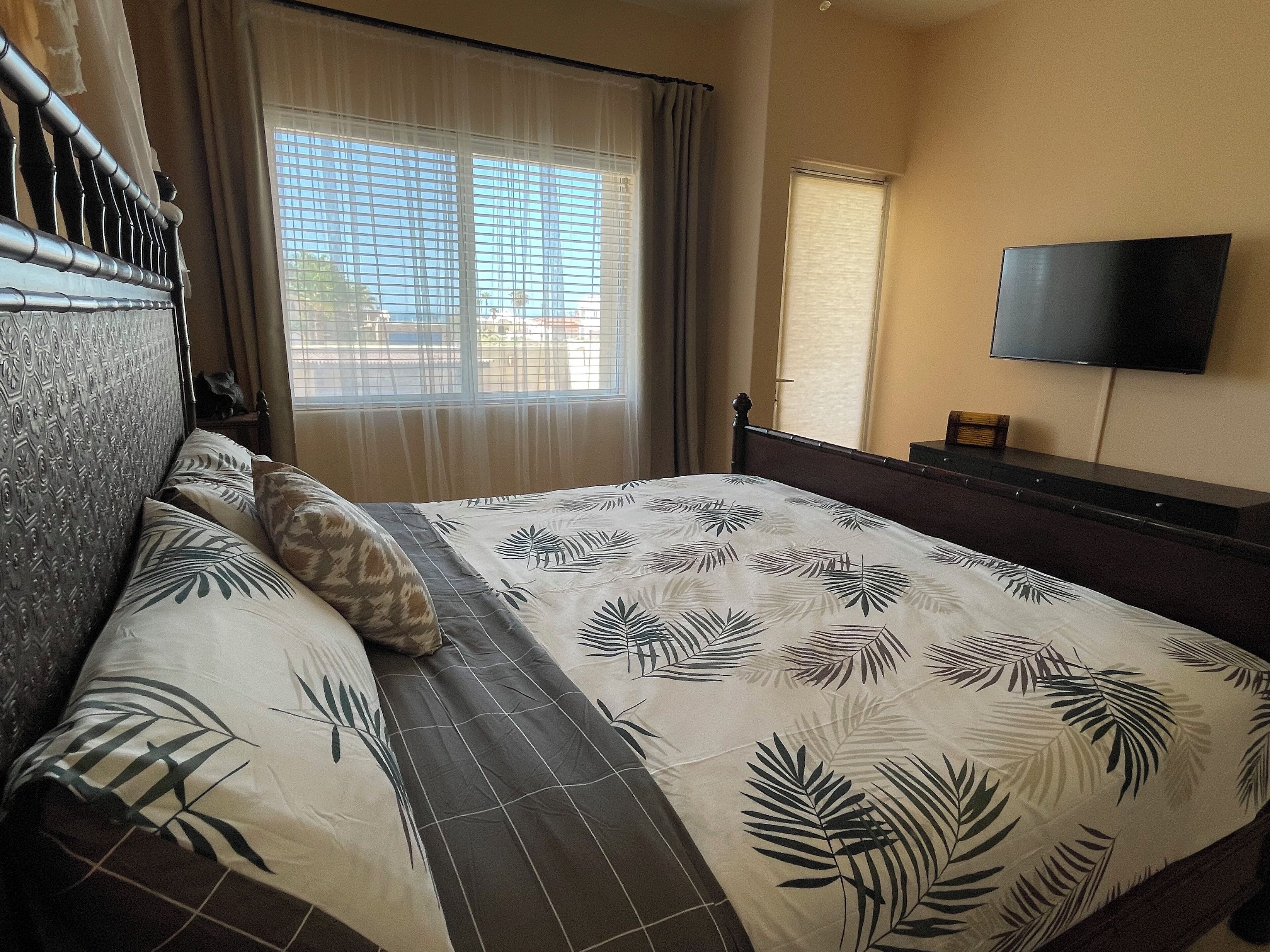 Habitación de hotel con cama, televisión montada en la pared y ventana con cortinas.