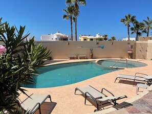 A swimming pool with lounge chairs, palm trees, and a building in the background. - Corona del Mar by Rocky Host (Puerto Peñasco)