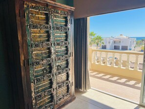A room with a large sliding door leading to a balcony with a view of a white building and palm trees. - Corona del Mar by Rocky Host (Puerto Peñasco)
