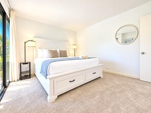 Une chambre à coucher avec un grand lit, des tables de chevet, une commode, un miroir et une vue par la fenêtre.