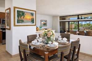 A dining area with a table set for six, surrounded by patterned chairs, with a view of the outdoors.
