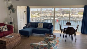 Un salon doté d’une grande fenêtre donnant sur une marina, d’un canapé bleu, d’un fauteuil rouge et d’une petite table avec des chaises.