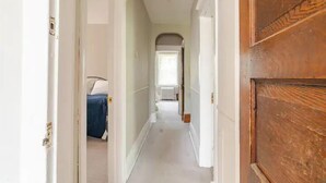 A narrow hallway with a wooden door on the right and a bed with a blue cover in the left room. - The Carew House Sleeps 10 Fenced 4BR Full Kitchen Steps2 YCP (York)