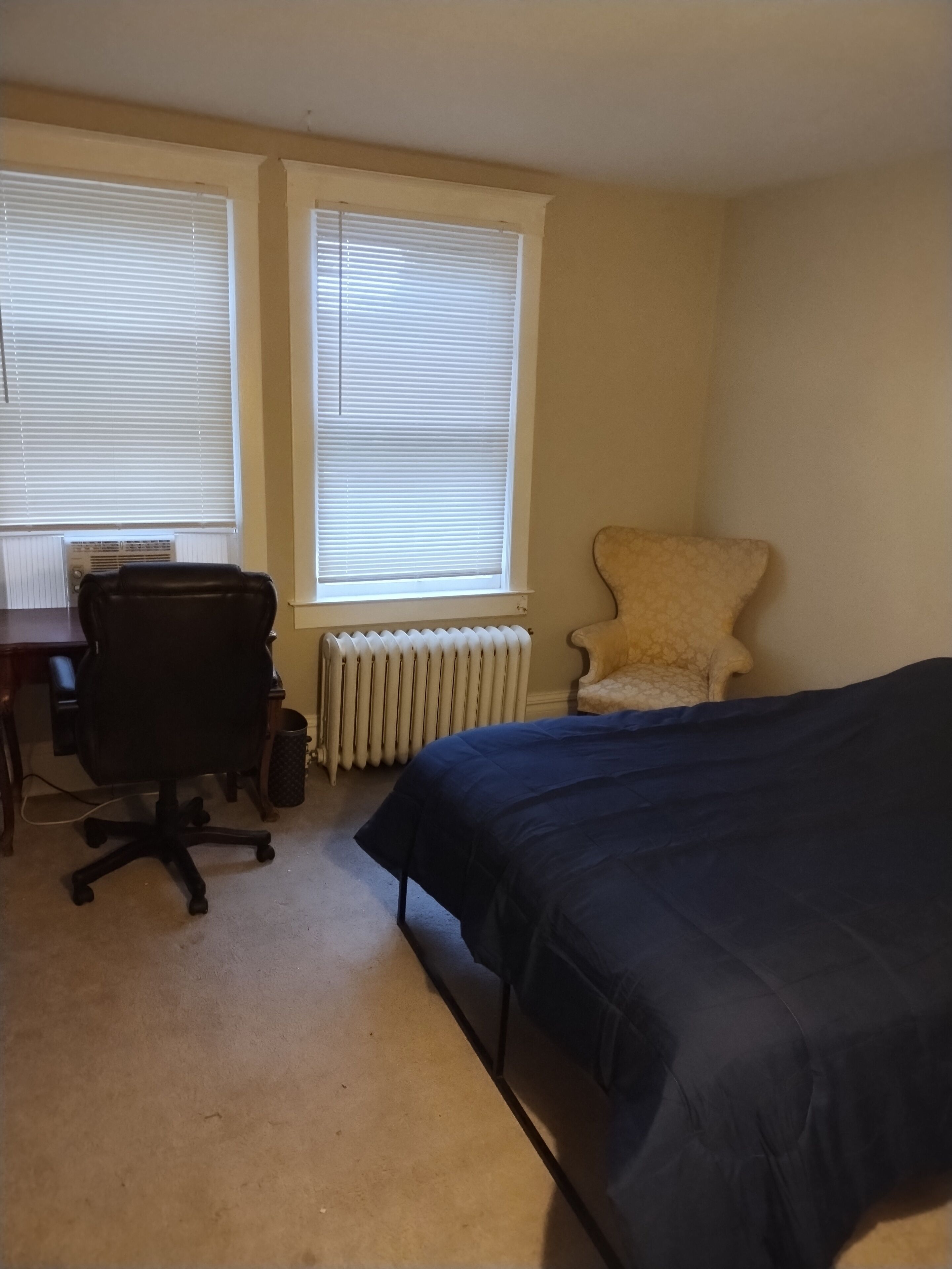 Une chambre à coucher avec un lit, une chaise, un bureau et un radiateur.