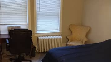 A bedroom with a bed, a chair, a desk, and a radiator.