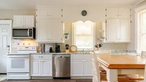 A modern kitchen with white cabinets, stainless steel appliances, and a wooden dining table. - The Carew House Sleeps 10 Fenced 4BR Full Kitchen Steps2 YCP (York)