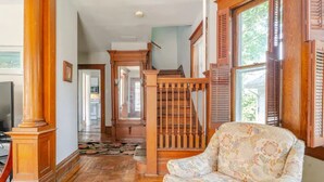 A spacious living room with a wooden staircase, a patterned armchair, and a view of the kitchen through an open door. - The Carew House Sleeps 10 Fenced 4BR Full Kitchen Steps2 YCP (York)