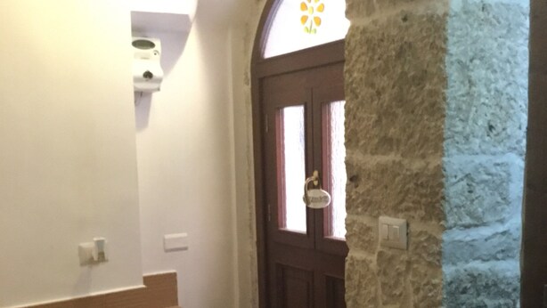 A staircase leading to a wooden door with a window, a stone wall, and a small window with a flower design.