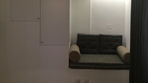 A small, dimly lit room with a single bed, a mirror, and a light fixture above the bed.