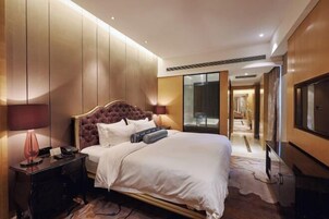 Una habitación de hotel con una cama grande, una mesita de noche con lámpara, un televisor y un armario.