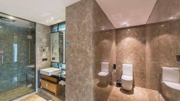 Un baño moderno con cabina de ducha de vidrio, un tocador con lavamanos y dos inodoros.