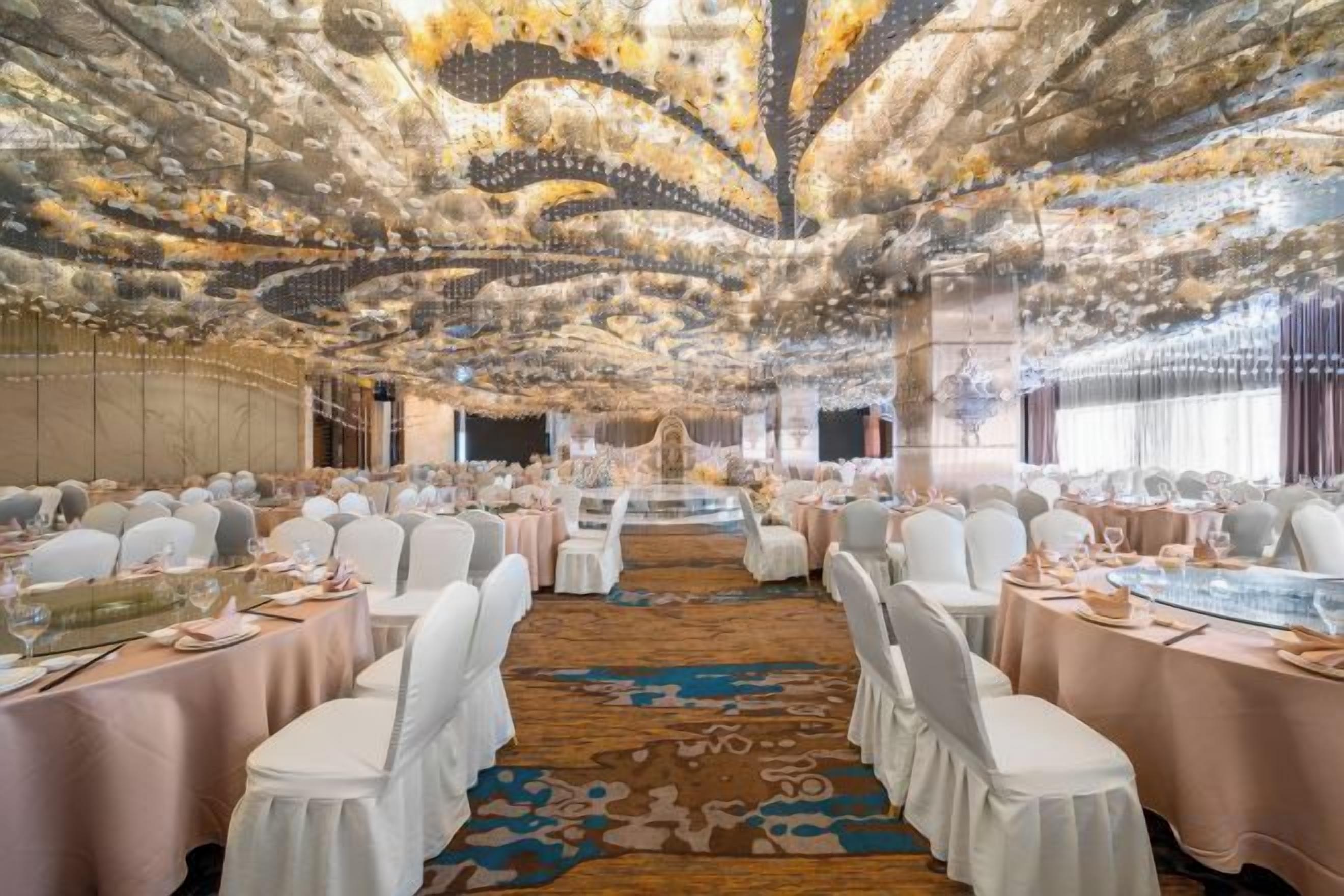 A banquet hall with round tables, white chairs, and a decorative ceiling.