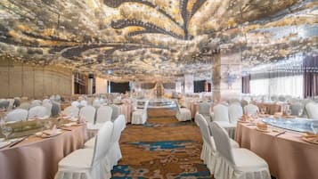 A banquet hall with round tables, white chairs, and a decorative ceiling.