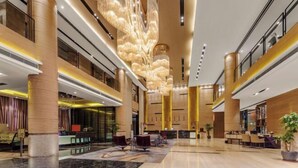Eine geräumige Lobby mit hoher Decke, großen Säulen und einem modernen Kronleuchter.