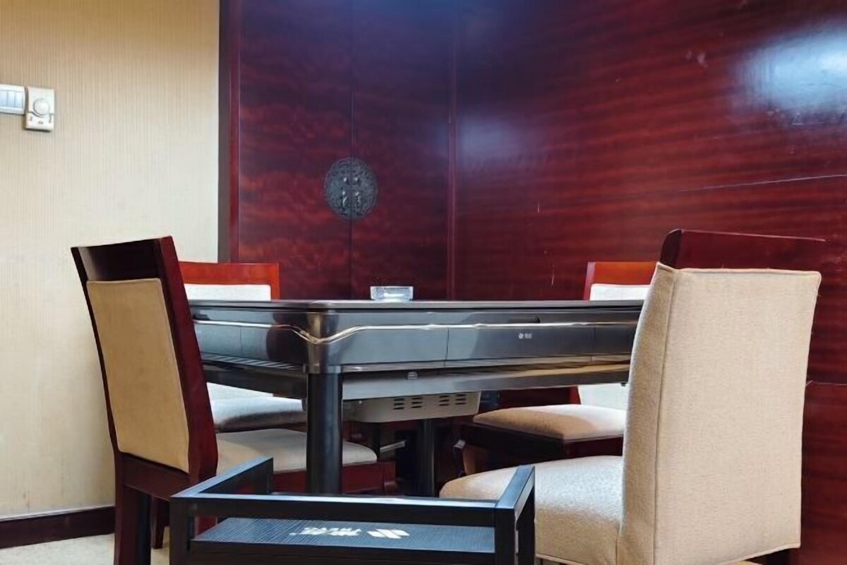 A conference room with a rectangular table and four chairs, a decorative wall panel, and a small round object on the wall.