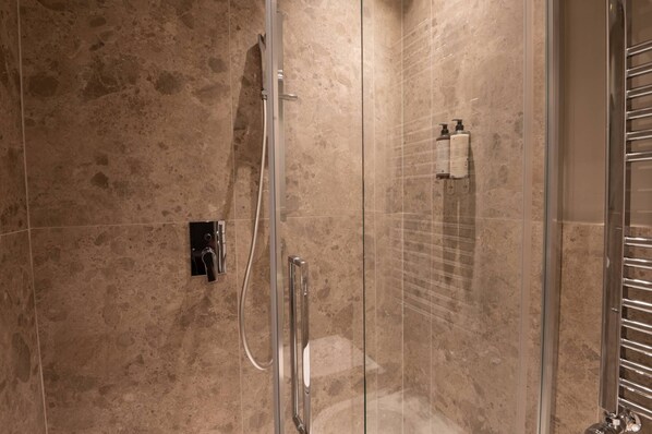 A glass-enclosed shower with a handheld showerhead and a wall-mounted control panel.