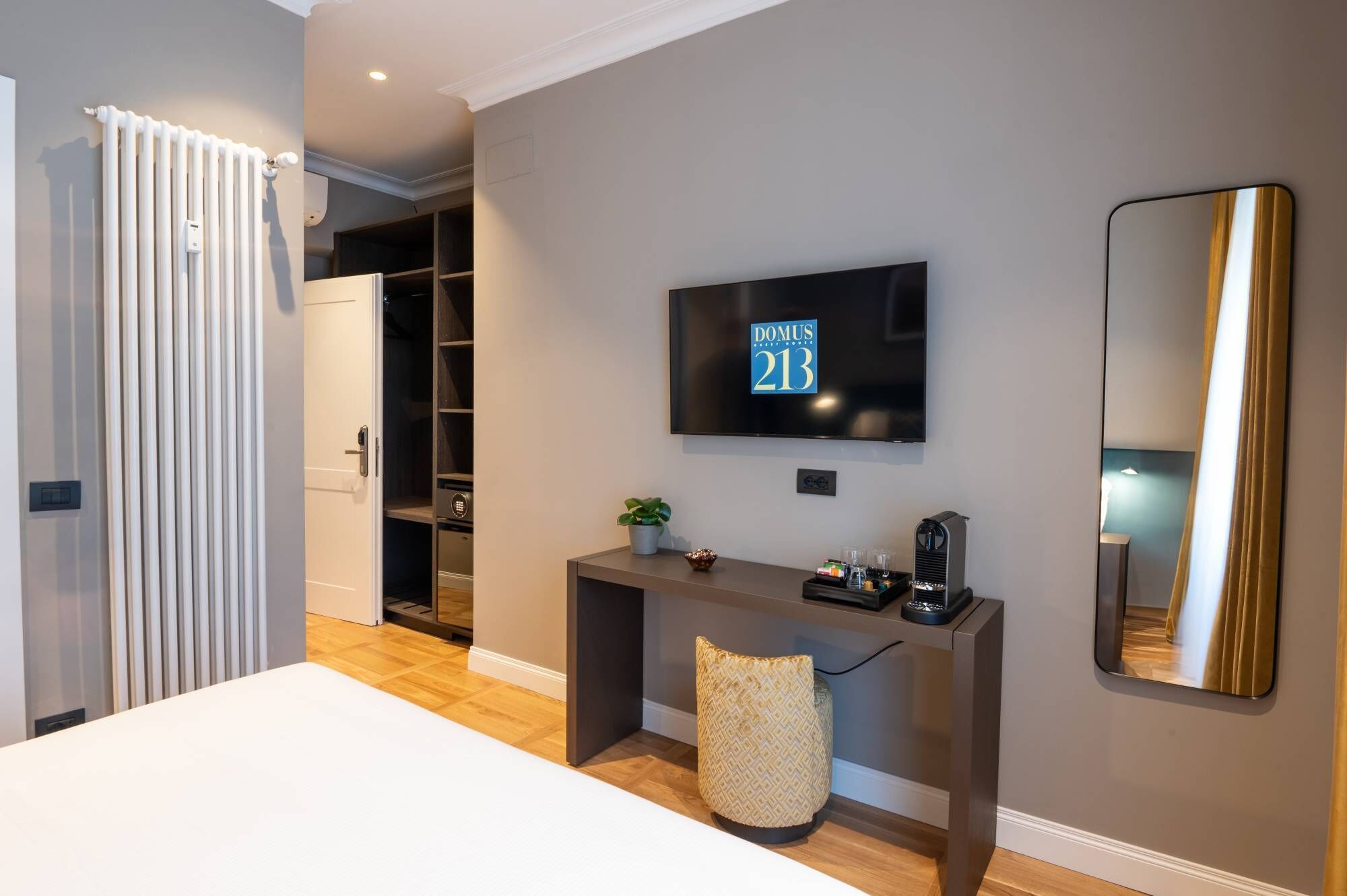 A modern hotel room with a large TV, a mirror, a desk, and a wardrobe.