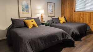 Une chambre avec deux lits, chacun recouvert d’une couvre-lit à motifs et agrémenté d’oreillers, une table de chevet avec une lampe, des tableaux encadrés au mur et une fenêtre avec des stores.