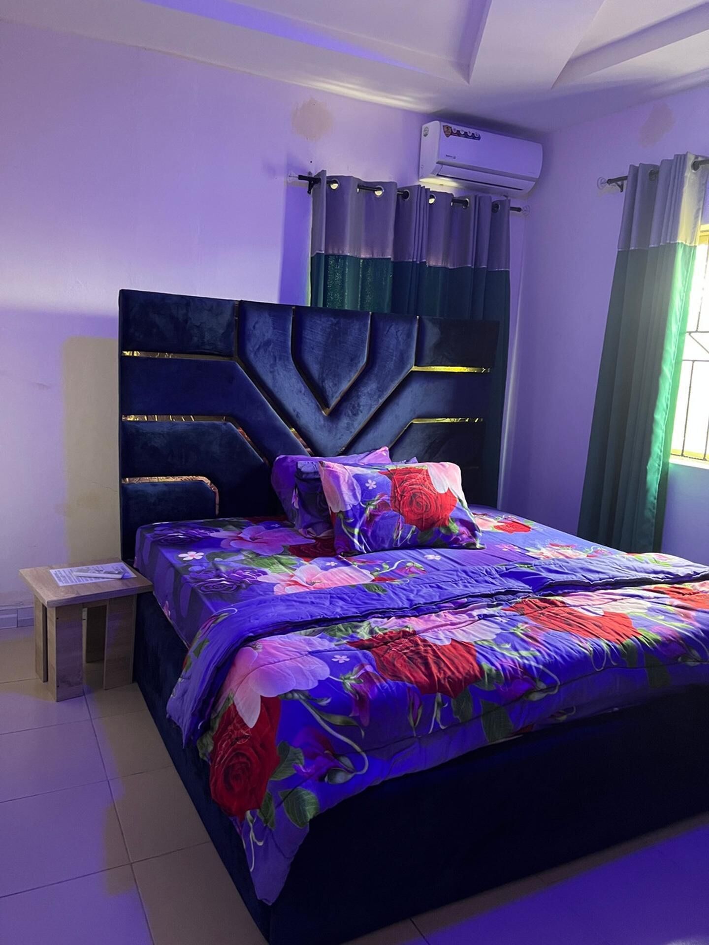 Une chambre à coucher comprenant un lit, une table de chevet, une fenêtre avec des rideaux et un appareil de climatisation.