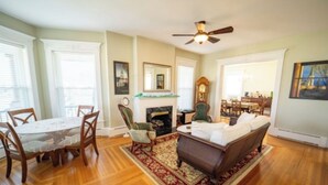 A living room with a fireplace, a sofa, a dining table with chairs, and a ceiling fan. - THE VICTORIAN GUESTHOUSE BED & BREAKFAST - Room 6 (Delphos)