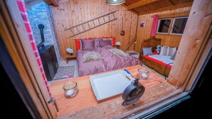 A cozy wooden cabin room with a bed, a small table, and a window. - Mazot Douillet de Montagne Isolé en Pleine Nature en Autonomie D'énergie (Les Giettes)