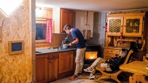 A cozy kitchen with wooden cabinets, a wood-burning stove, and a dining area with a rocking chair. - Mazot Douillet de Montagne Isolé en Pleine Nature en Autonomie D'énergie (Les Giettes)