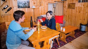 A wooden interior with a dining table, chairs, a red cushion, and a wooden wall with a clock and framed pictures. - Mazot Douillet de Montagne Isolé en Pleine Nature en Autonomie D'énergie (Les Giettes)