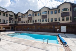 A swimming pool with a wooden deck, surrounded by a building with multiple windows and balconies. - Walk to Festivals and Lift 7 | Remodeled 3BR Condo | Hot Tub + Garage Parking (Telluride)