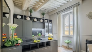 Een moderne keuken met grijze kastjes, een zwart aanrecht en een groot raam met gordijnen.