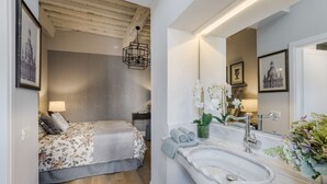 Een slaapkamer met een bed, een nachtkastje, een hanglamp en een grote spiegel boven de wastafel.