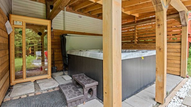 A wooden cabin with a hot tub, a glass door entrance, and a small outdoor seating area. - Havre de Détente & Spa (Sainte-Lucie-des-Laurentides)
