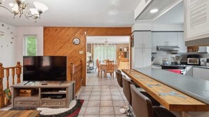 A modern kitchen with a built-in oven, microwave, and stove. There is a dining area with a wooden table and chairs. A TV is placed on a wooden stand in the living area. - Havre de Détente & Spa (Sainte-Lucie-des-Laurentides)