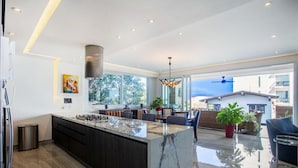 Una cocina moderna con una isla de mármol, armarios oscuros y un amplio ventanal con vistas al exterior.