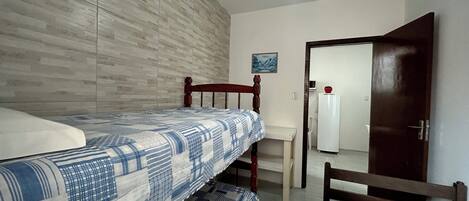 A bedroom with two beds, a ceiling fan, a white door, and a small table.