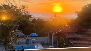 Een uitzicht op de zonsondergang boven de oceaan, een zwembad en een gebouw met een betegeld dak.