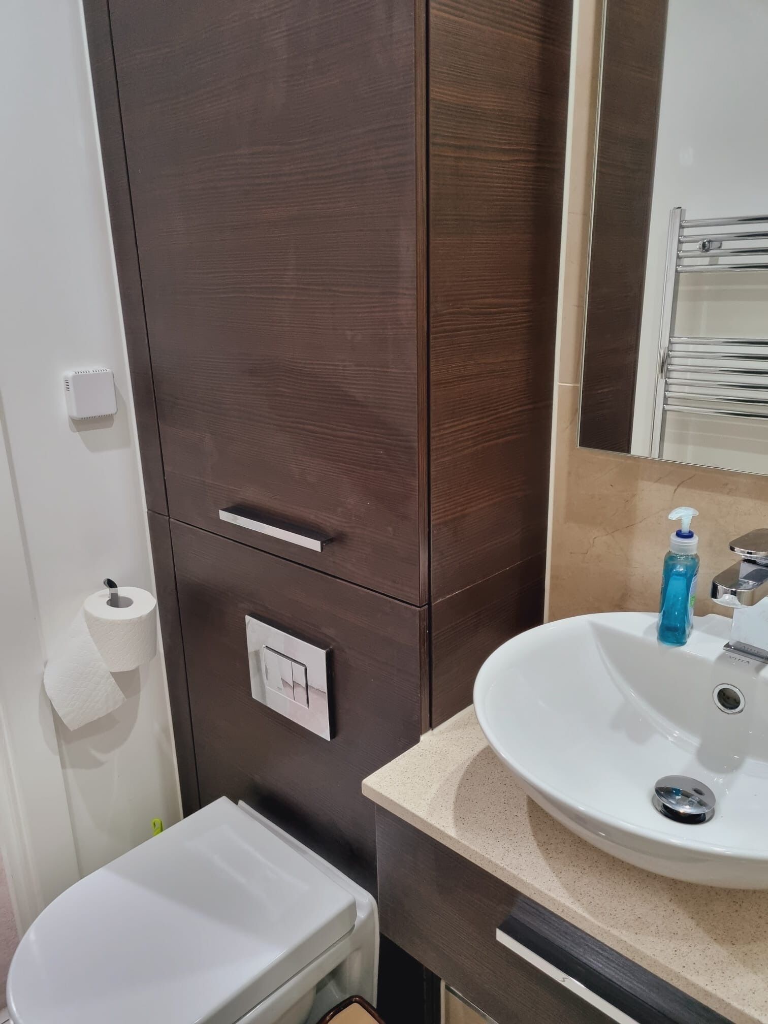 A bathroom with a white sink, a mirror, a dark wooden cabinet, and a toilet.