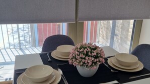 Ruokapöytä on katettu lautasilla, kulhoilla ja aterimilla, ja pöydän keskellä on maljakko, jossa on kukkia.