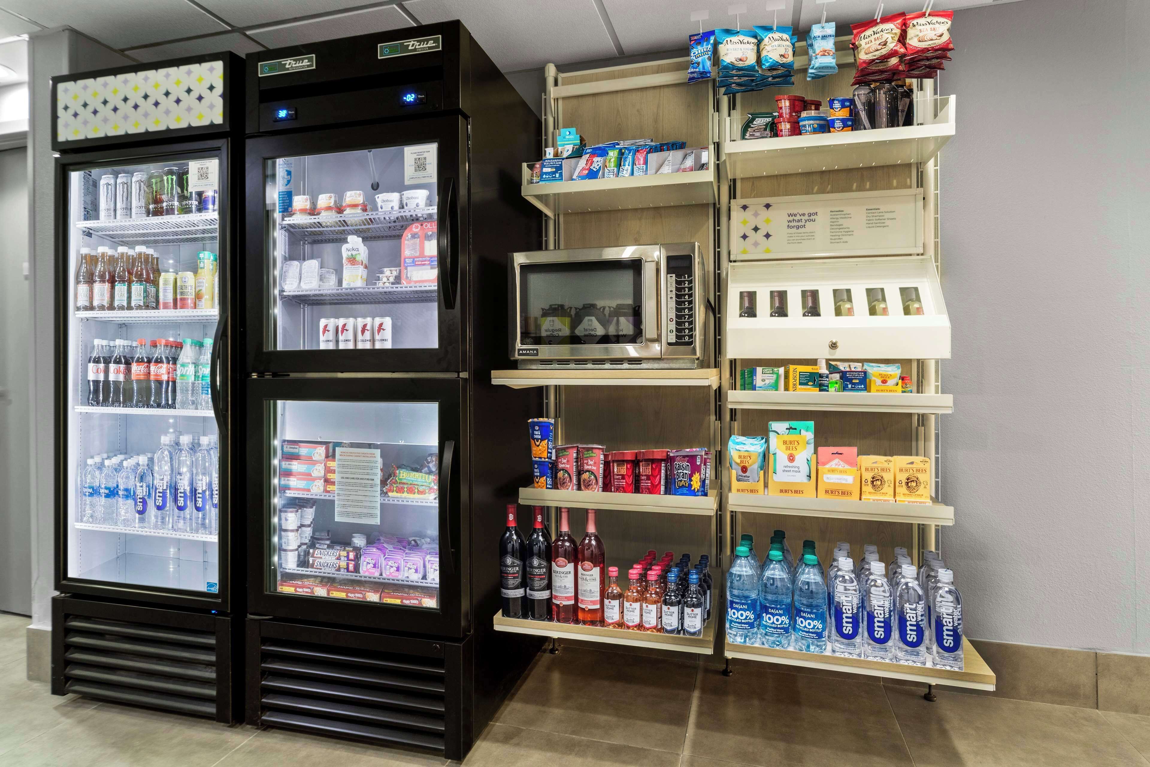 A vending machine with beverages and snacks, a microwave, and shelves with various packaged goods.