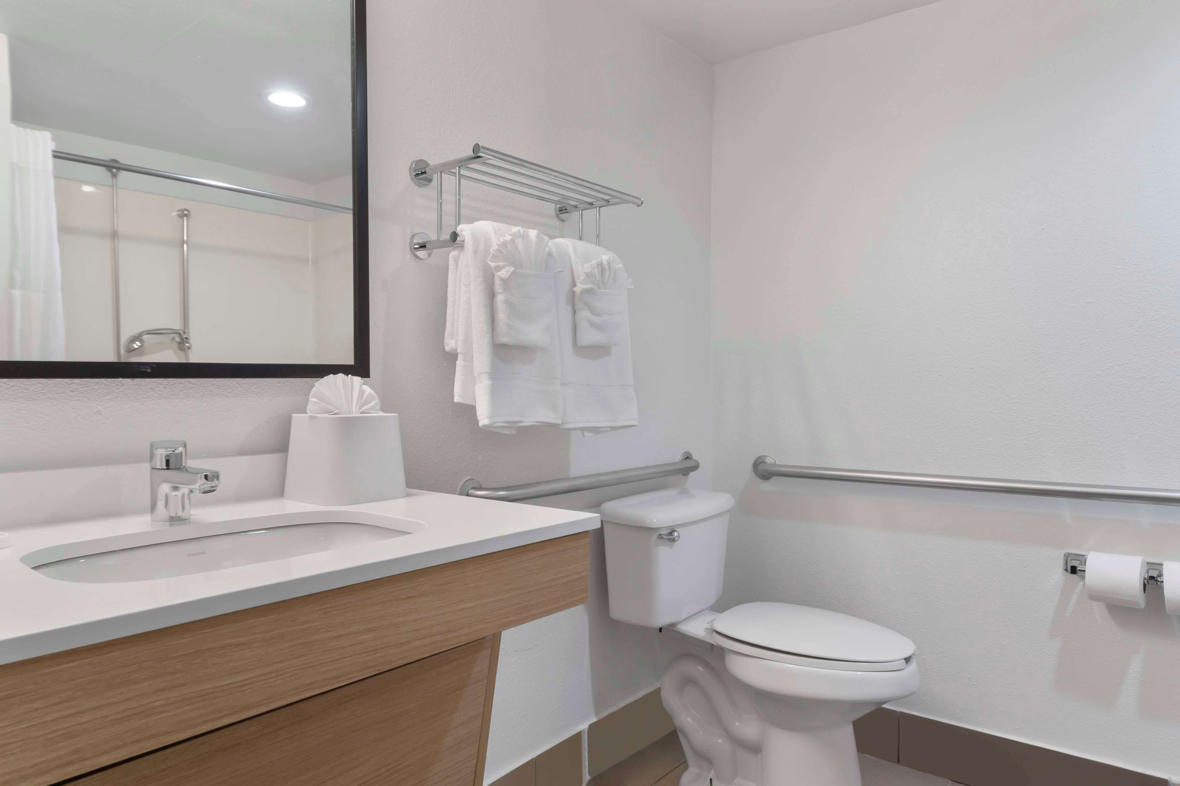 Un baño moderno con lavamanos, inodoro y barras de apoyo.