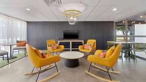 A modern meeting room with yellow rocking chairs, a central table, and a large flat-screen TV on the wall. - Spark By Hilton Grand Prairie (Grand Prairie)