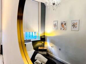 Relax in a stylish room with a large bed, bedside table, and chandelier, offering a city view.