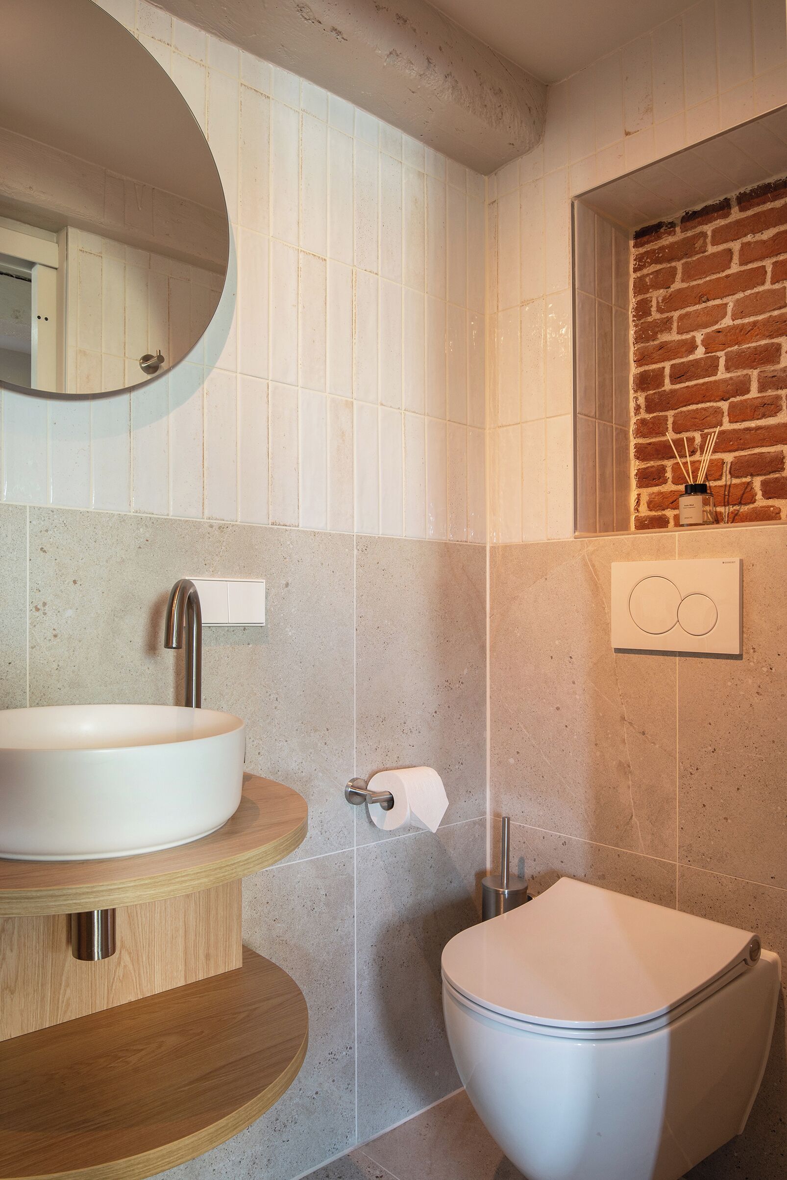 A modern bathroom with a round mirror, a white sink, and a toilet.