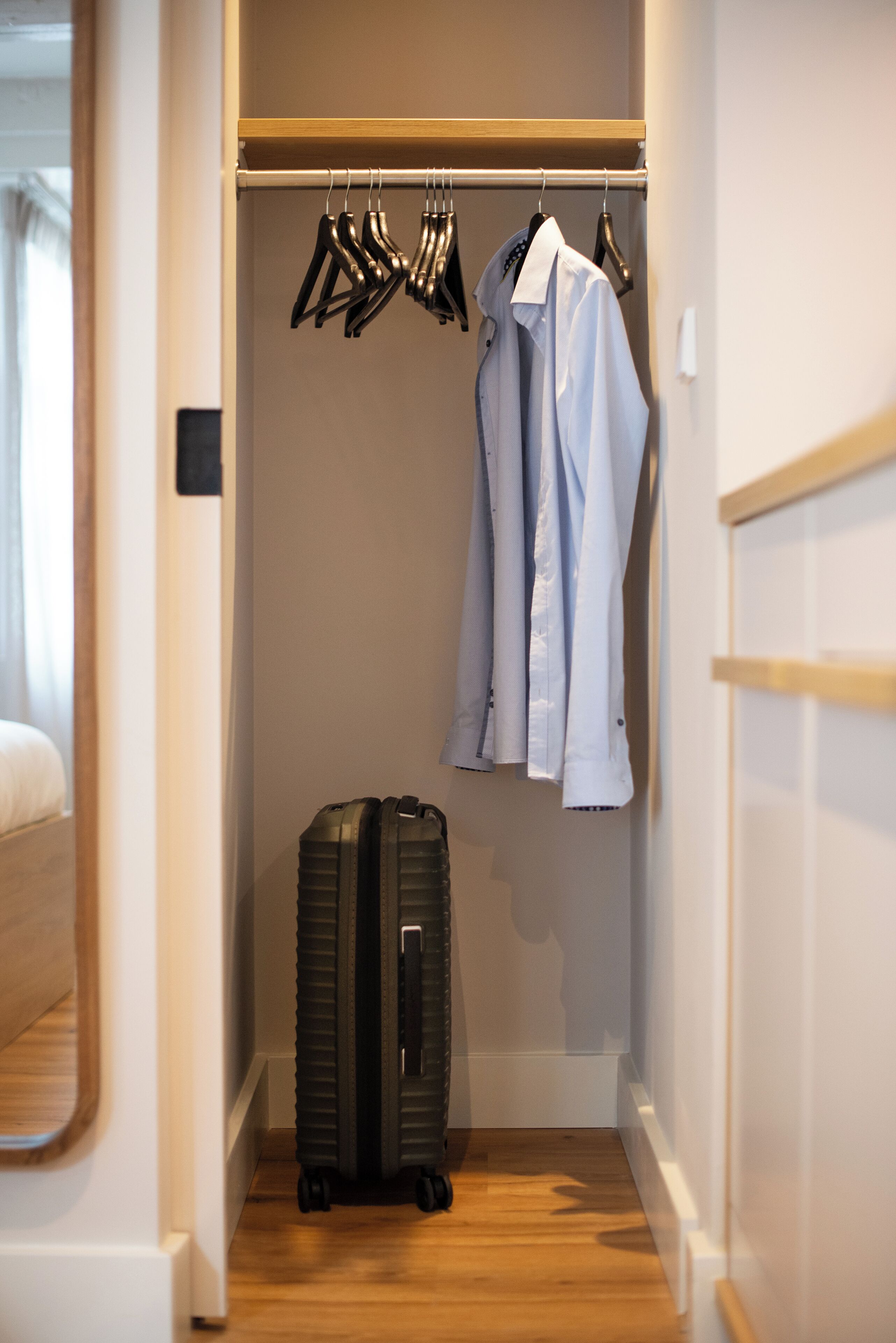 Een hotelkamer met een houten vloer, een kast met hangende kleding en een koffer.