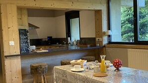Una cocina acogedora y rústica con vigas de madera, un comedor con mantel estampado y vistas al verdor exterior.