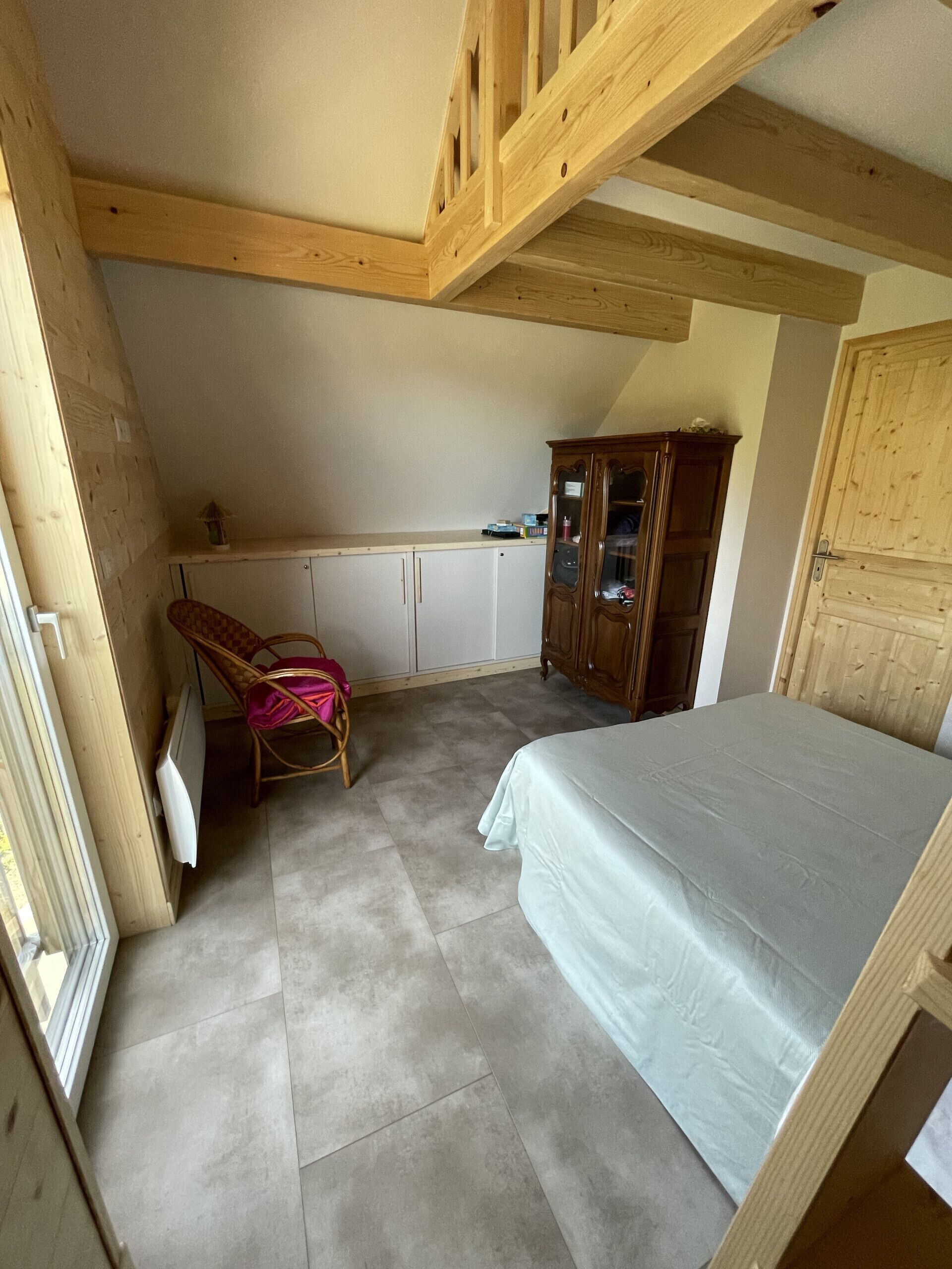 Een slaapkamer met een bed, een houten garderobe, een stoel en een klein tafeltje.